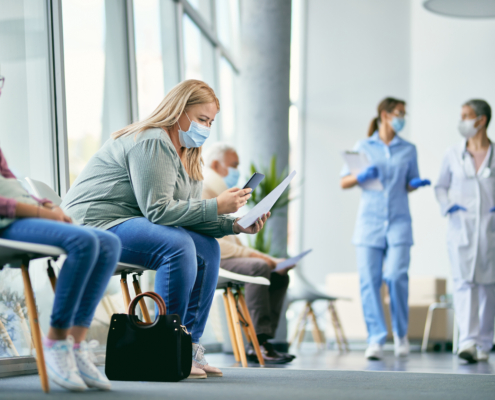 Woman with face mask using smart phone while reading her medical report in waiting room at the clinic.